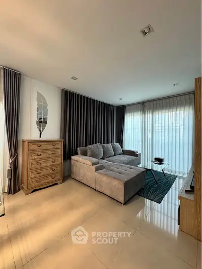 Modern living room with plush gray sofa, elegant curtains, and natural light for a cozy ambiance.