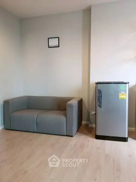 Modern living room with sleek gray sofa and compact fridge, perfect for urban living.