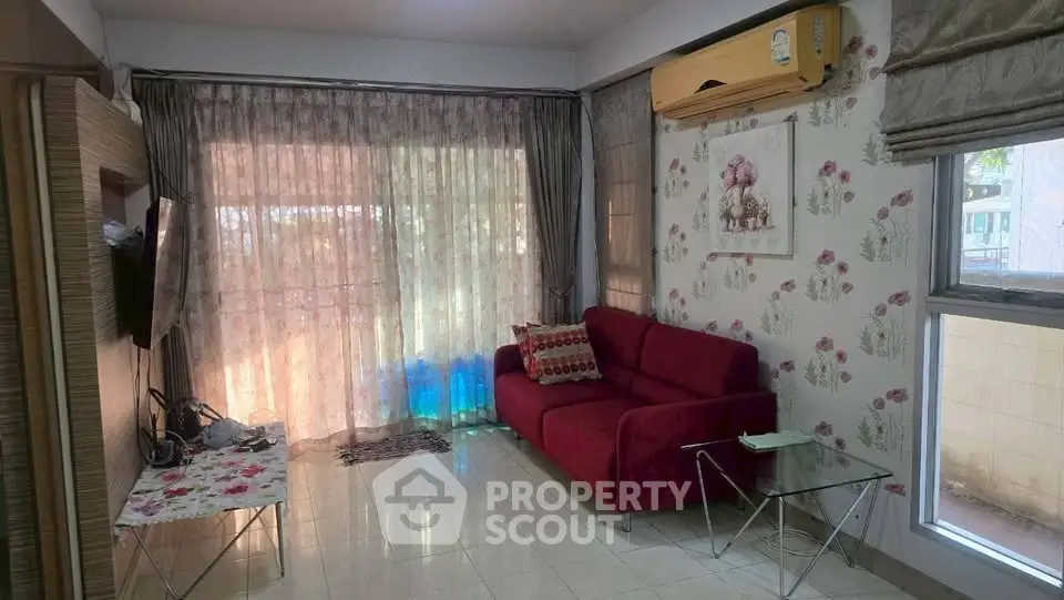 Cozy living room with red sofa and floral wallpaper, featuring large windows and natural light.