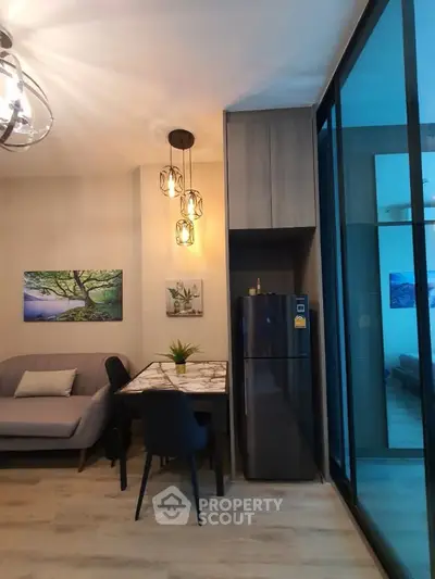 Modern living room with stylish decor and dining area, featuring elegant lighting and a sleek refrigerator.