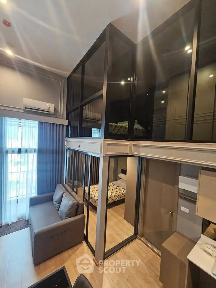 Modern loft-style living room with high ceilings and glass-enclosed bedroom, featuring sleek furniture and natural light.