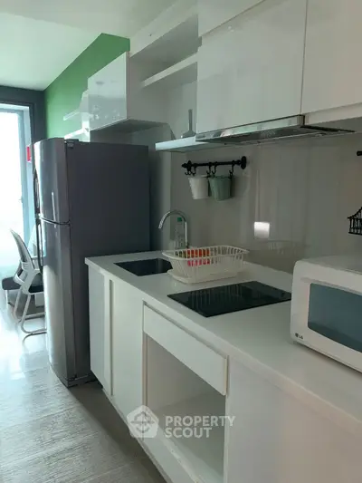 Modern kitchen with sleek white cabinetry and appliances, featuring a fridge and microwave.