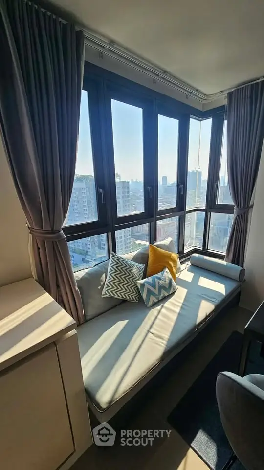 Bright corner unit with large windows offering stunning city views, featuring cozy seating area with stylish cushions.