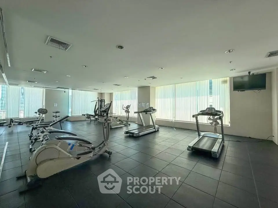 Spacious gym with modern equipment and large windows offering city views.