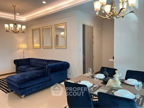 Elegant living and dining area with plush blue sofa and stylish chandeliers.
