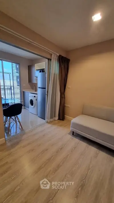 Modern apartment with open layout, featuring a cozy living area and a kitchen with a washing machine and fridge.