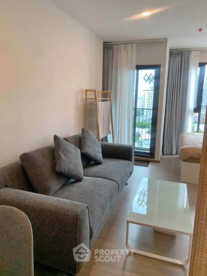 Modern living room with gray sofa and large windows offering city views in a stylish apartment.