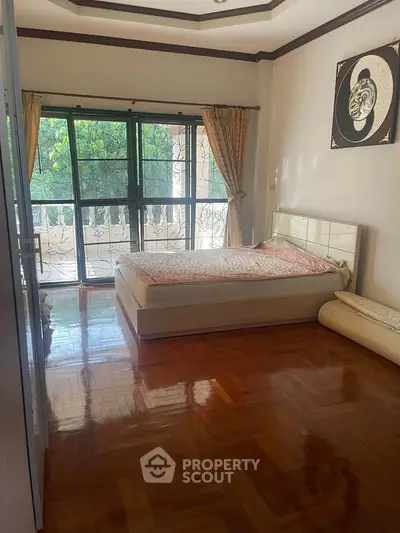 Spacious bedroom with large windows and balcony access, featuring elegant wooden flooring and stylish decor.