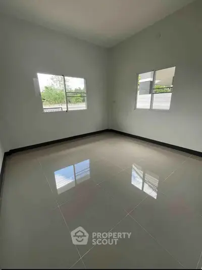 Spacious empty room with glossy tiled floor and large windows offering natural light.