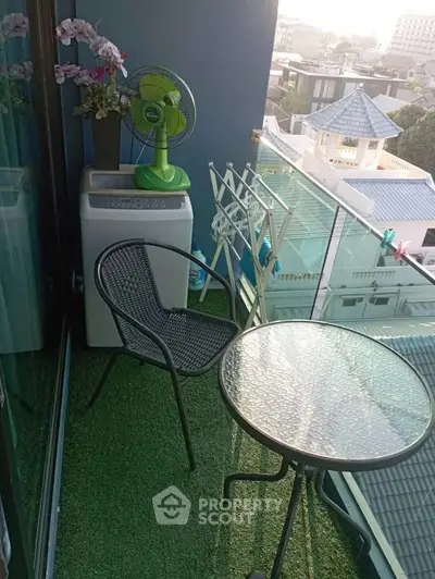 Charming balcony with city view, featuring a glass table, chair, and washing machine, perfect for relaxation.