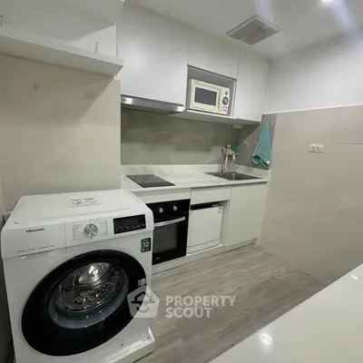 Modern kitchen with sleek appliances and compact design, featuring a washing machine and microwave.