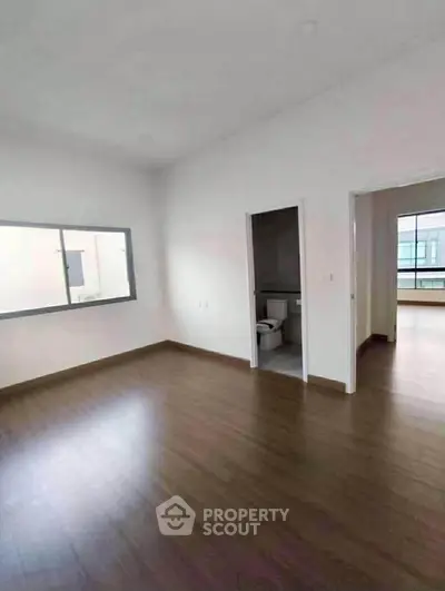 Spacious unfurnished room with wooden flooring and large window, ideal for customization.