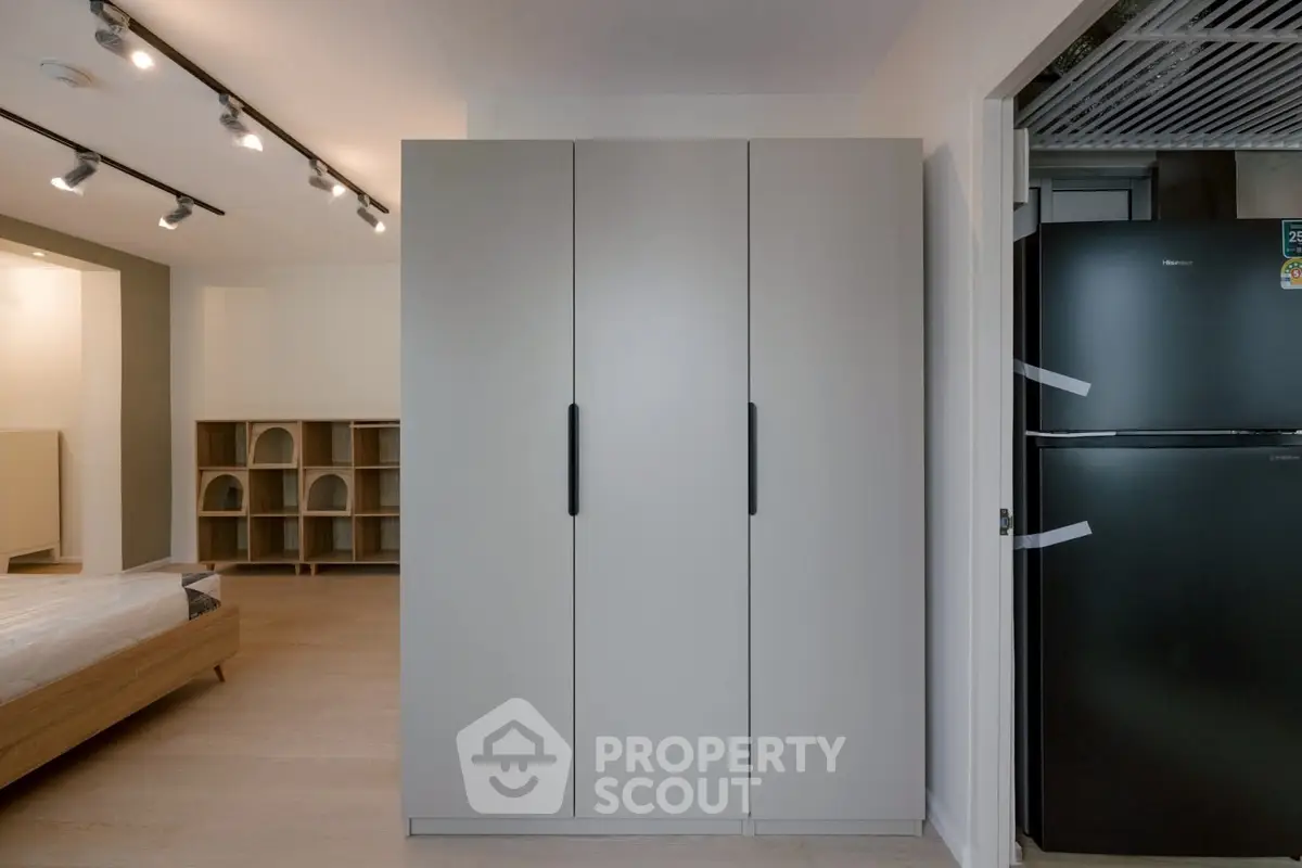 Modern bedroom with sleek wardrobe and black refrigerator, showcasing contemporary design.