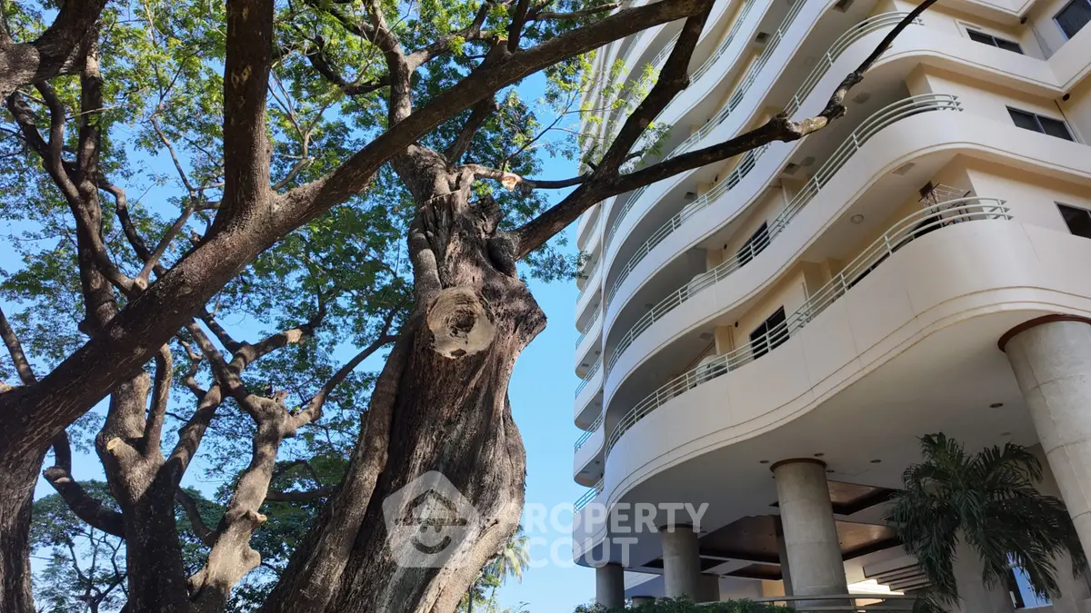 Modern building exterior with lush trees and clear blue sky, showcasing urban nature harmony.
