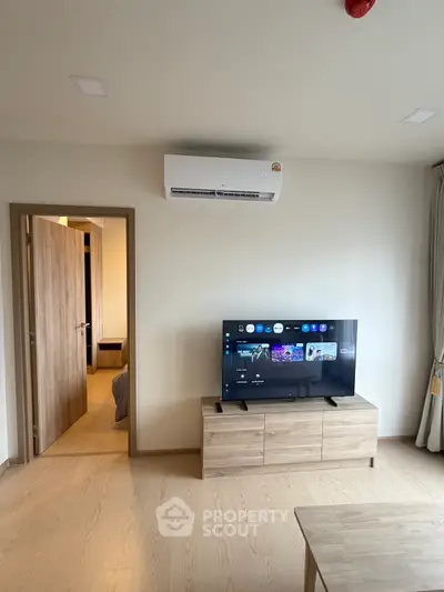 Modern living room with air conditioning and flat-screen TV, featuring wooden flooring and neutral decor.