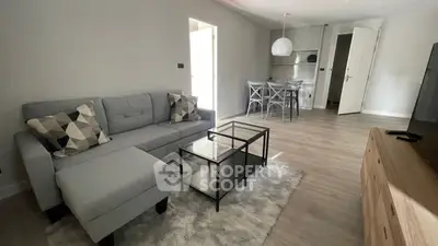 Spacious modern living room with elegant grey sectional sofa, sleek black coffee table, and an open layout leading to a well-equipped kitchen.
