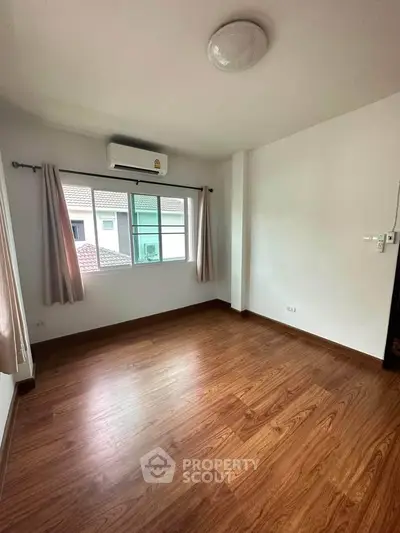 Spacious empty room with wooden flooring and large window, perfect for customization.