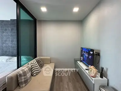 Modern living room with cozy sofa and TV, adjacent to a bedroom with glass partition.