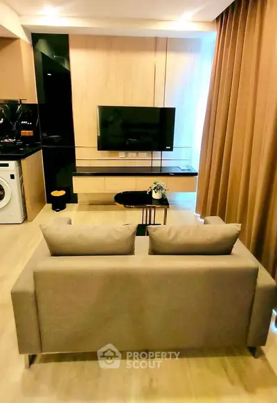 Modern living room with sleek TV setup and cozy sofa, featuring a washing machine in the corner.
