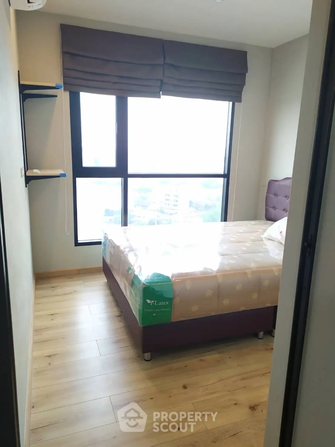 Cozy bedroom with large window offering city views, featuring modern furnishings and wooden flooring.