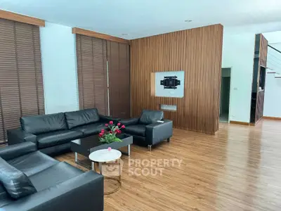 Spacious modern living room with sleek black leather sofas and elegant wooden accents.