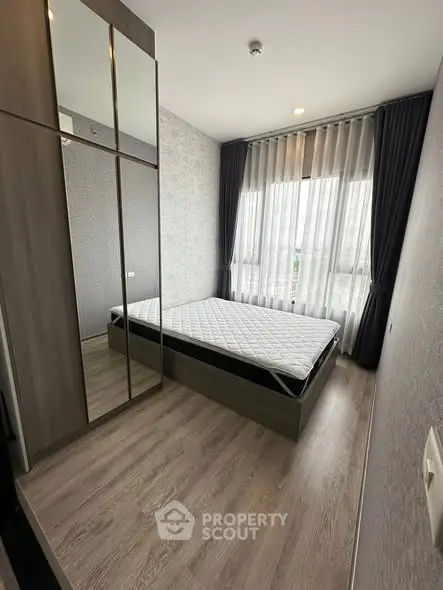 Modern bedroom with large window and mirrored wardrobe in stylish apartment.