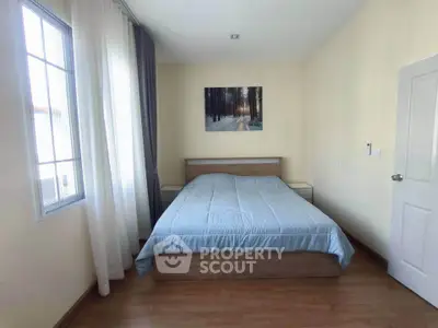 Cozy bedroom with wooden flooring and large window for natural light