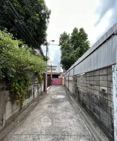 Narrow alleyway leading to residential property with lush greenery and secure gate.