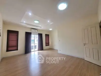 Spacious empty room with wooden flooring and large windows, perfect for customization.