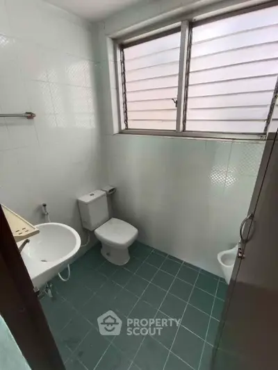 Compact bathroom with green tiled floor and frosted window for privacy.