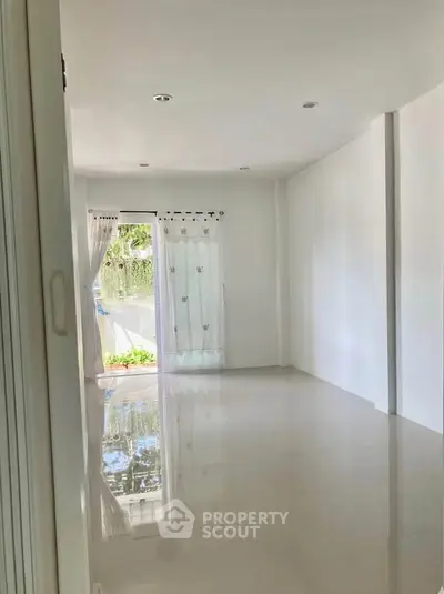 Spacious empty room with glossy white tiles and natural light from large window.