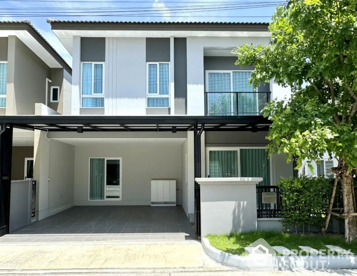 Modern two-story house with a spacious driveway and lush greenery, featuring a sleek balcony and contemporary design.