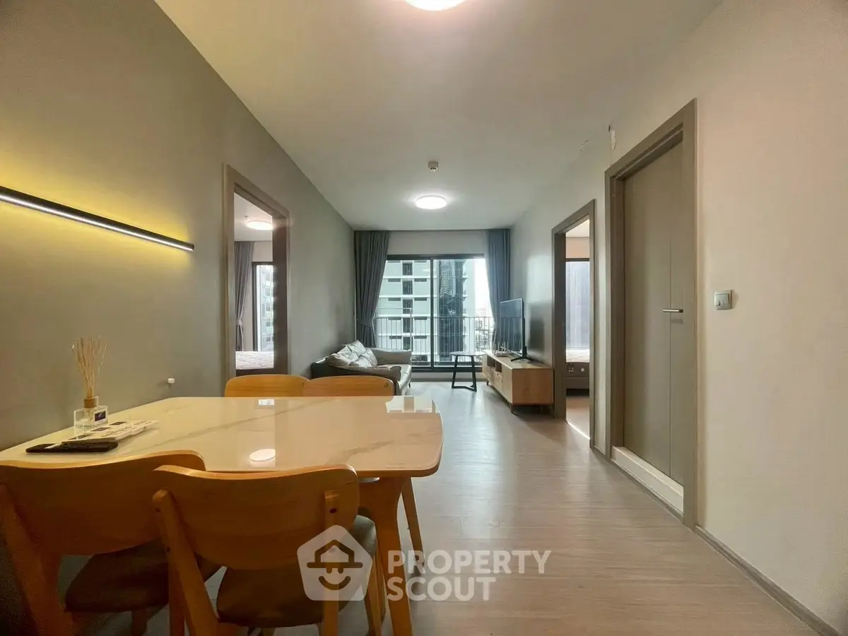 Modern apartment interior with open living and dining area, featuring wooden furniture and large windows.