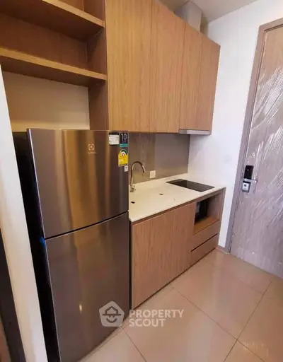 Modern compact kitchen with sleek cabinetry and stainless steel fridge in a stylish apartment.