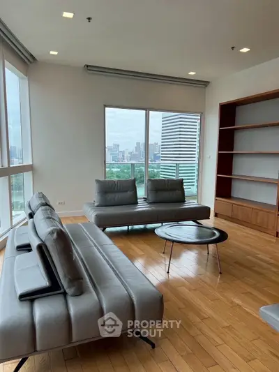 Spacious modern living room with city view, featuring sleek furniture and wooden flooring.