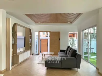 Modern living room with sleek furniture and large windows overlooking a garden, featuring a stylish wooden ceiling.