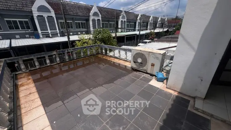 Spacious balcony with tiled flooring and air conditioning unit, overlooking a row of modern townhouses.