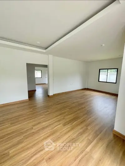 Spacious empty living room with wooden flooring and large windows in modern home.