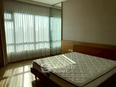 Spacious bedroom with large window and natural light, featuring a comfortable mattress and elegant curtains.