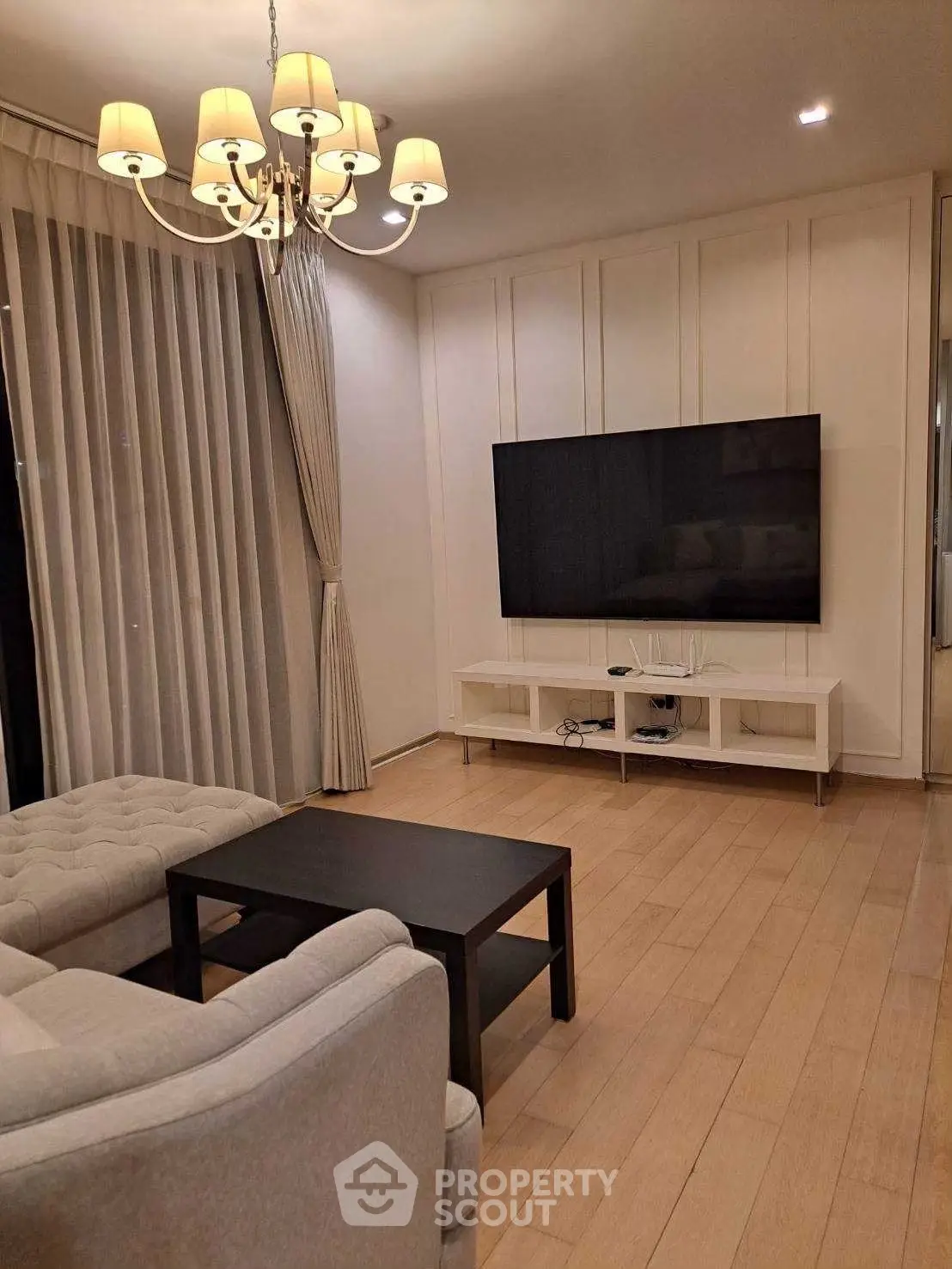 Elegant living room with modern decor, featuring a large flat-screen TV and stylish chandelier lighting.