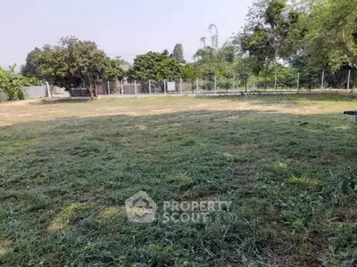 Spacious green plot of land with trees and fencing, ideal for development or landscaping.