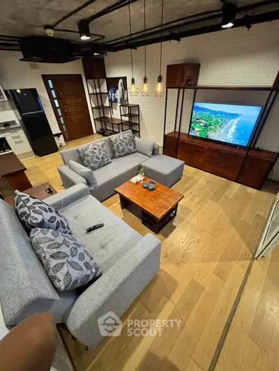 Stylish living room with modern furniture and wooden flooring, featuring a cozy seating area and a large TV.