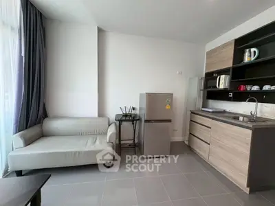 Modern studio apartment with sleek kitchen and cozy living area, featuring a fridge and stylish sofa.