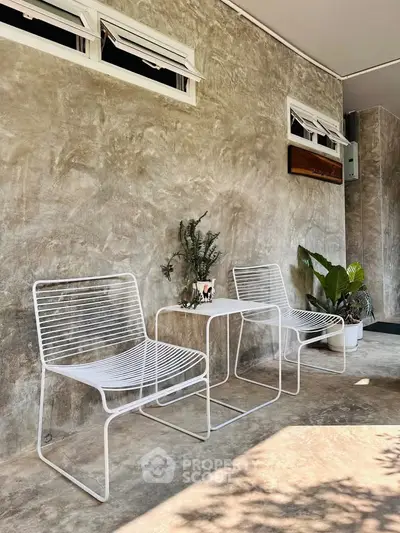 Chic outdoor seating area with modern white chairs and table on a stylish concrete patio.