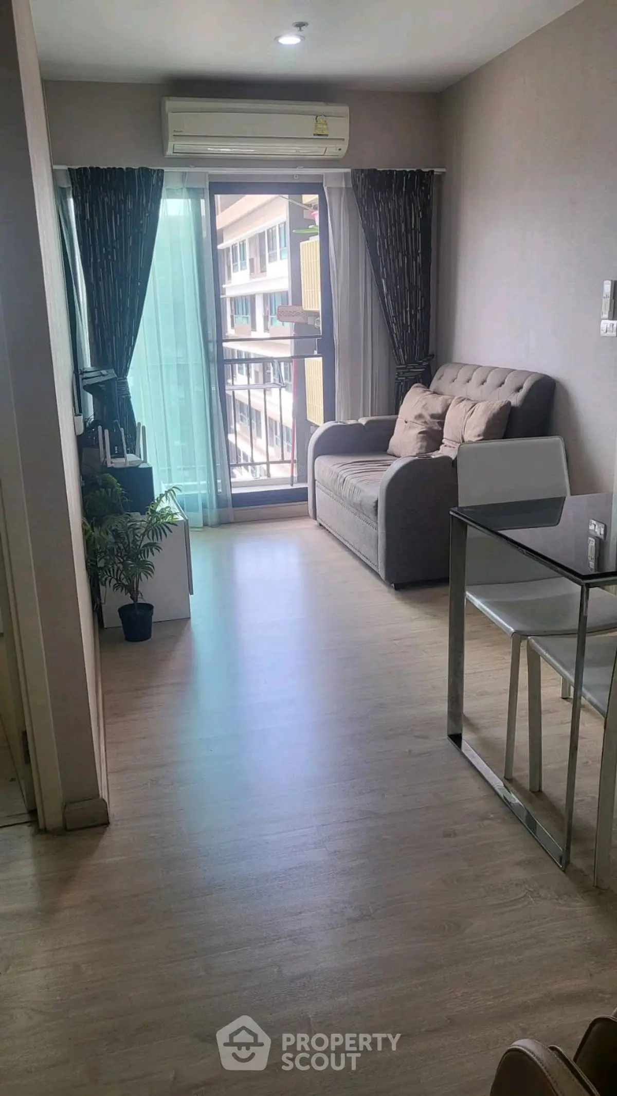 Modern living room with glass table and cozy sofa, featuring a balcony view.