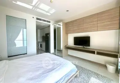 Modern bedroom with built-in TV unit and partial kitchen view in a bright apartment.
