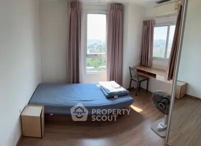 Cozy bedroom with city view, featuring a bed, desk, and large windows for natural light.