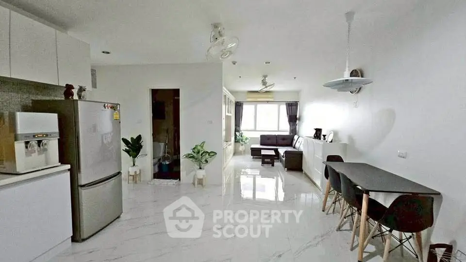 Spacious modern living room with open kitchen and dining area, featuring sleek white interiors and natural light.