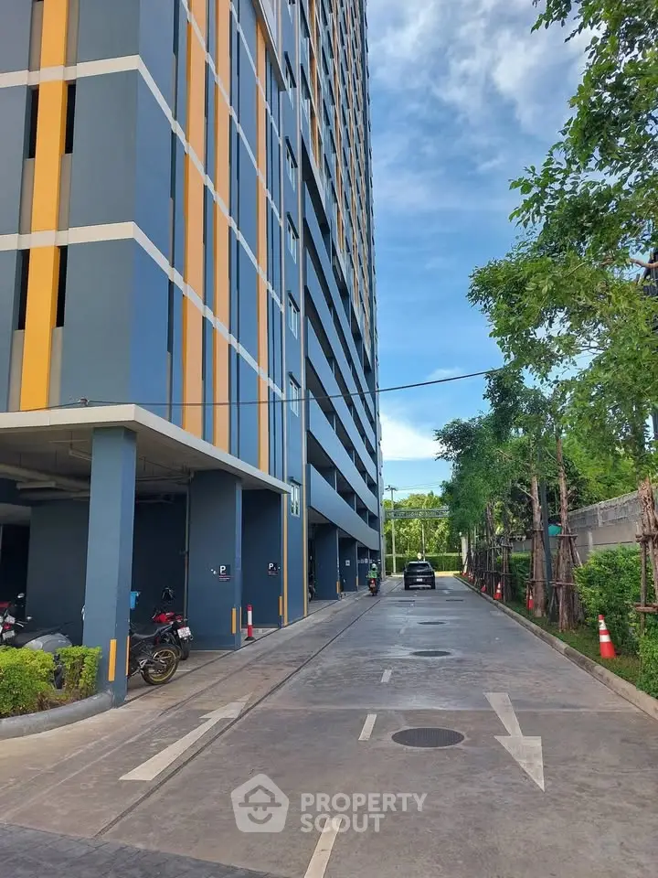 Modern high-rise building exterior with parking area and lush greenery