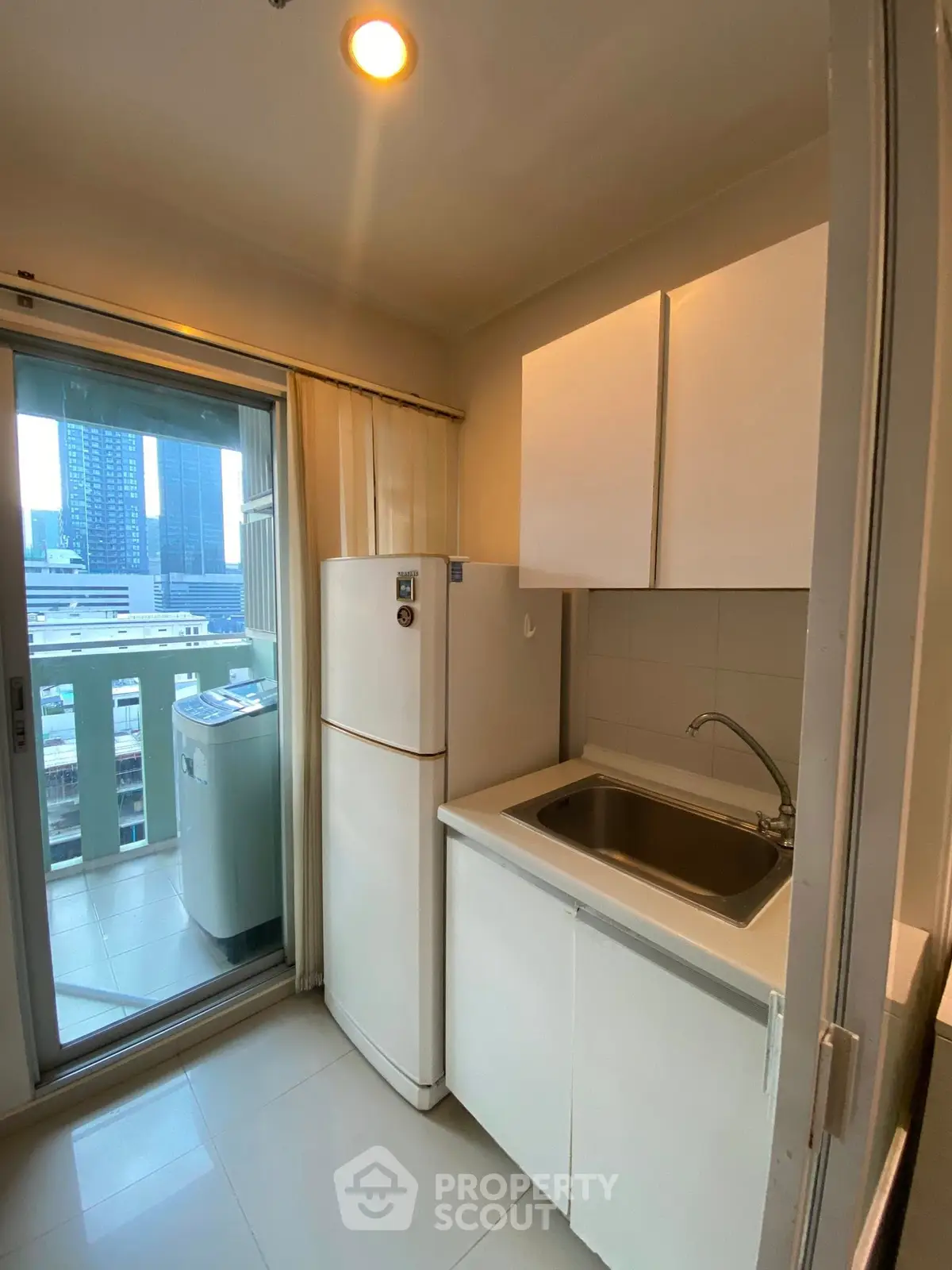 Compact kitchen with balcony view, featuring a fridge and washing machine.